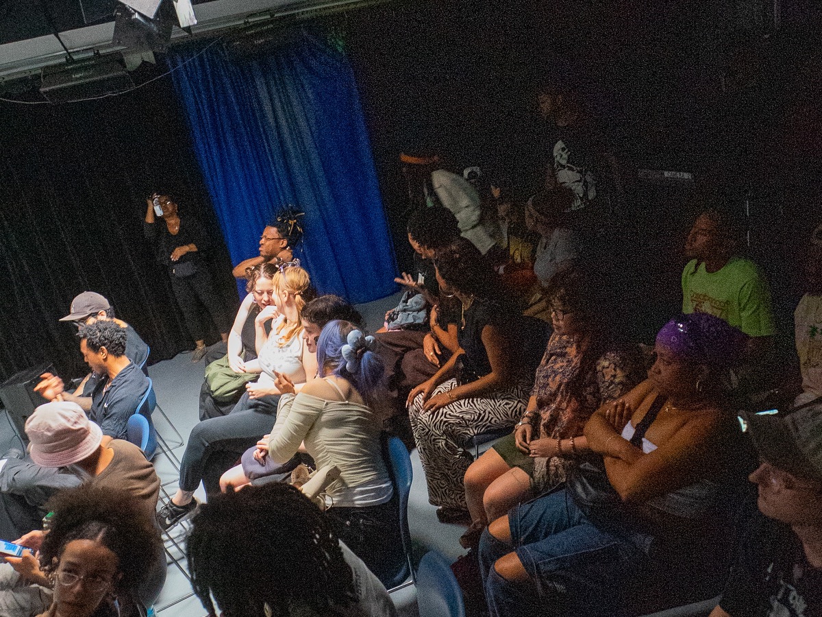 Audience members gather in a dark performance space with a blue curtain during the canna&cid album listening release at BRIC Arts & Media