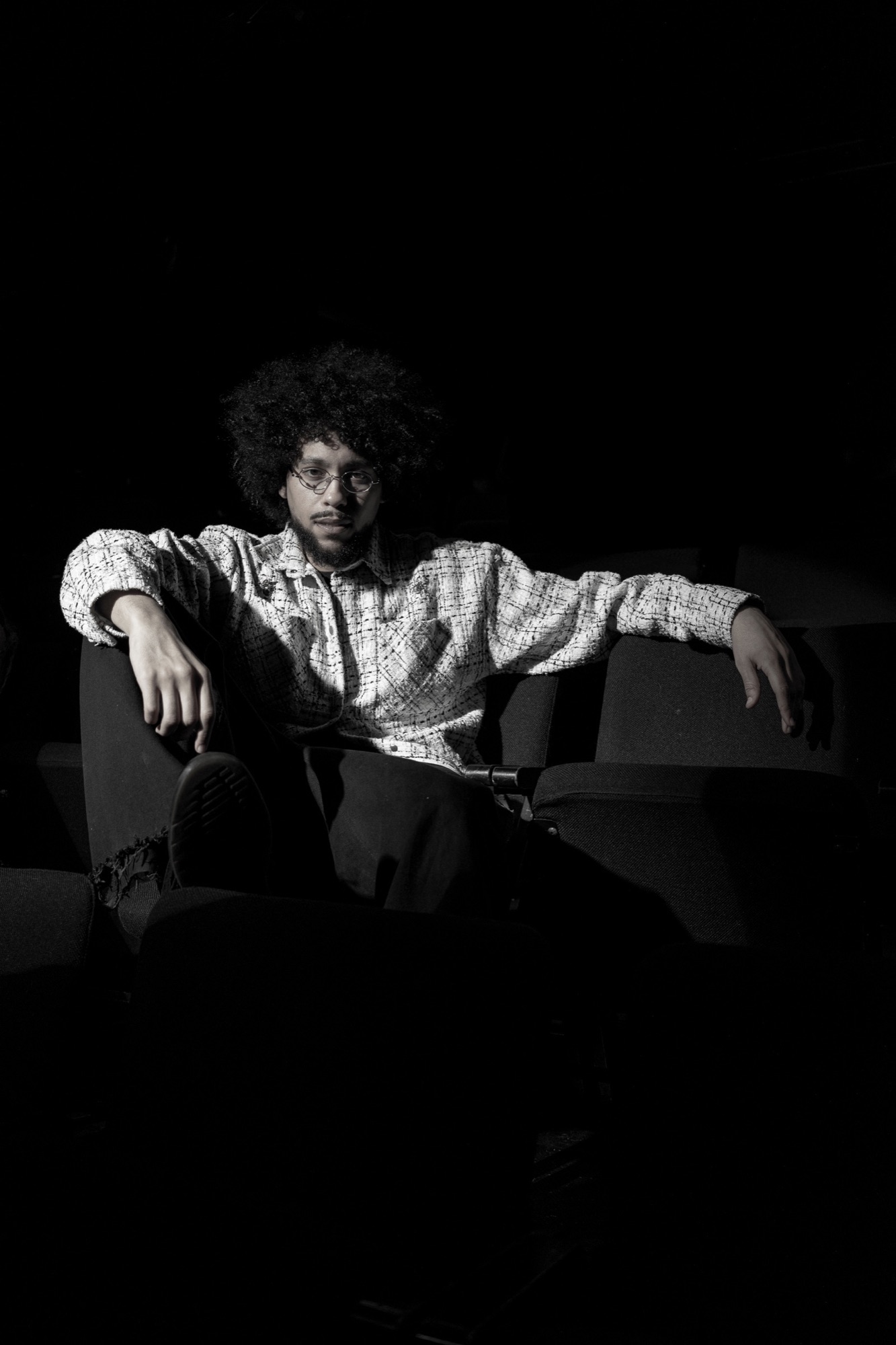 Chikadibia Ebirim seated between theater chairs under a narrow light