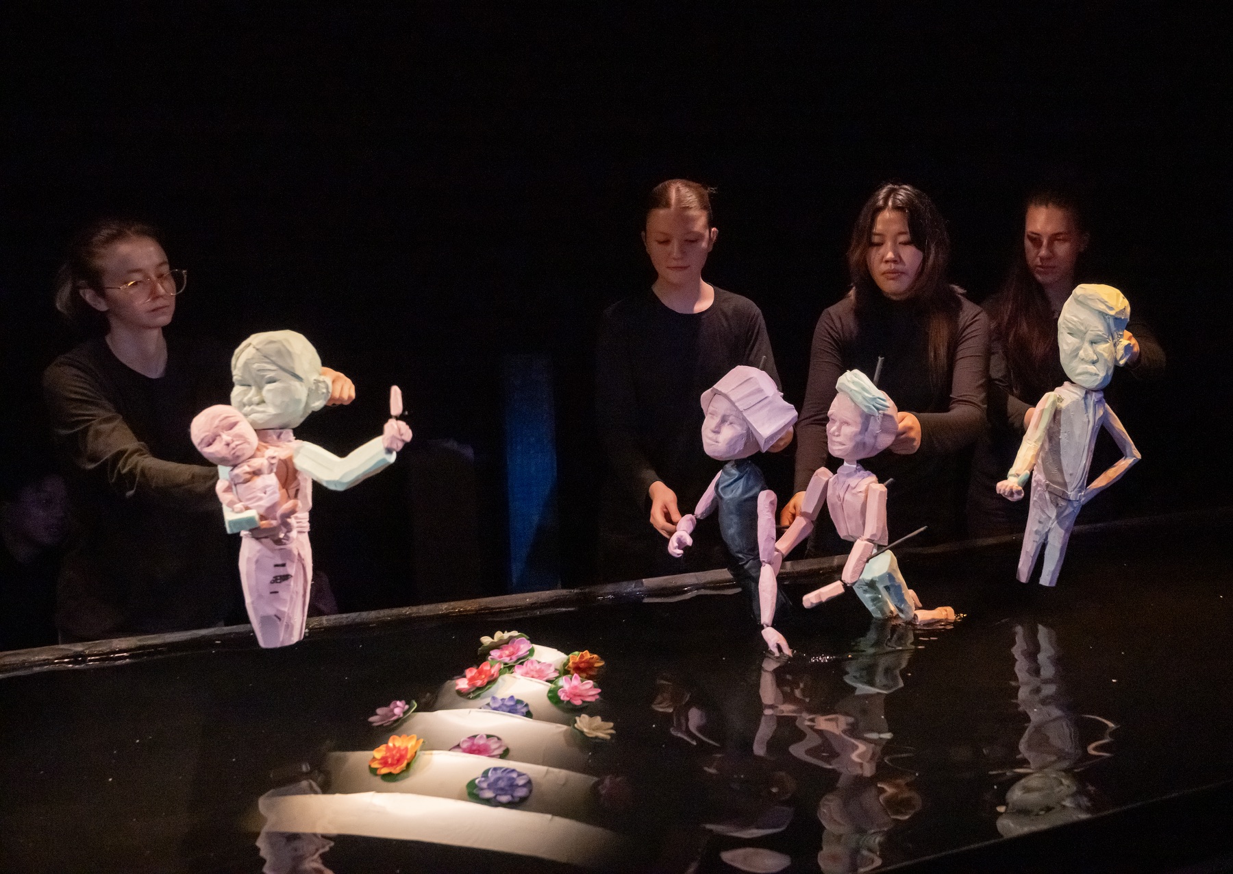 Four puppeteers performing The Magnificent Ms. Pham around its water stage